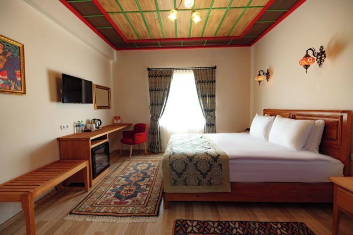Une chambre à coucher avec un lit, un bureau, une chaise, un téléviseur et une fenêtre avec des rideaux.