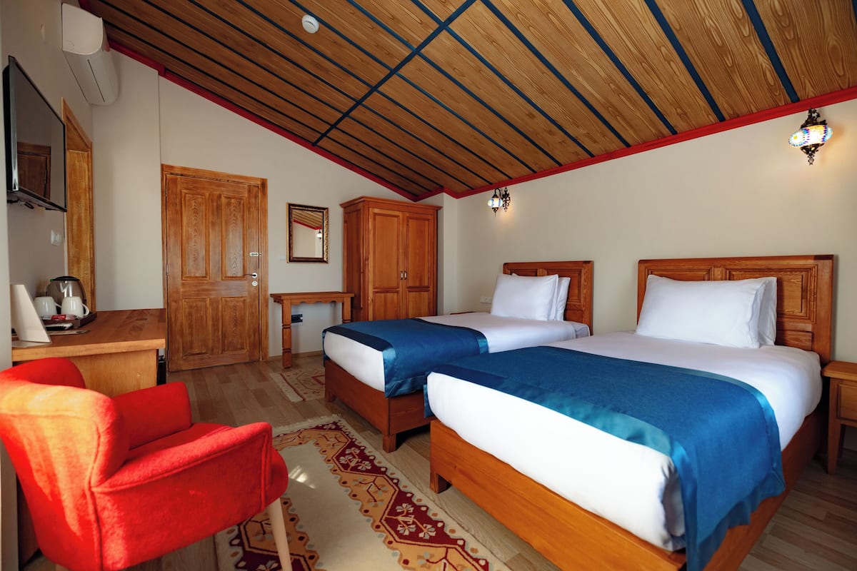 Een kamer met twee bedden, een houten bureau, een rode stoel en een plafond met houten balken.