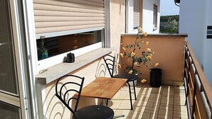 A balcony with a table and chairs, a potted plant with yellow flowers, and a view of a green landscape. - Gemütliche Ferienwohnung Belvie in Pohl-göns (Butzbach)