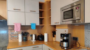 A modern kitchen with white cabinets, a stainless steel microwave, a coffee maker, and a knife block. - Gemütliche Ferienwohnung Belvie in Pohl-göns (Butzbach)