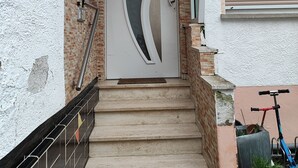 A modern house entrance with a white door, a brick wall, and a metal staircase. - Gemütliche Ferienwohnung Belvie in Pohl-göns (Butzbach)