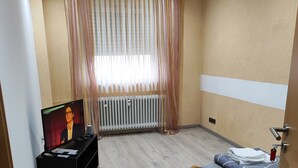 A room with a bed, a TV, a radiator, and a window with curtains. - Gemütliche Ferienwohnung Belvie in Pohl-göns (Butzbach)
