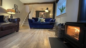 Una sala de estar acogedora con un sofá azul, un sofá de cuero marrón, una chimenea y una escalera que sube a otra habitación.