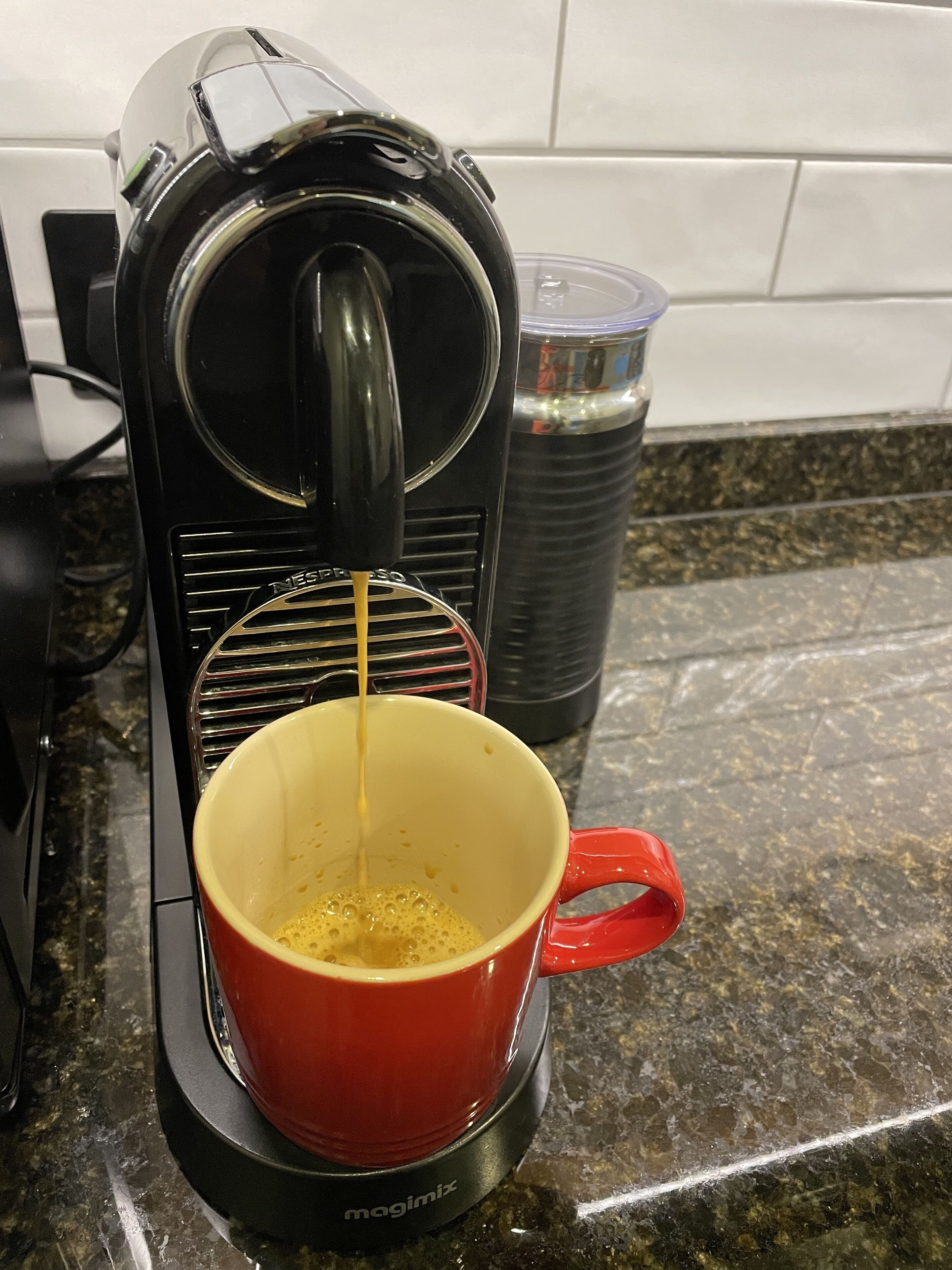 Eine Kaffeemaschine auf einer Küchenarbeitsplatte, davor eine rote Tasse.