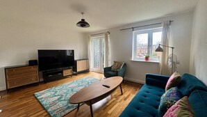 Ein Wohnzimmer mit Fernseher, Sofa und einem großen Fenster.