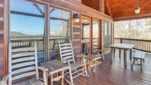 A wooden deck with a table and chairs, large windows, and a hanging light fixture. - Gorgeous Blue Ridge Mountain Retreat: Deck + View! (Blue Ridge)