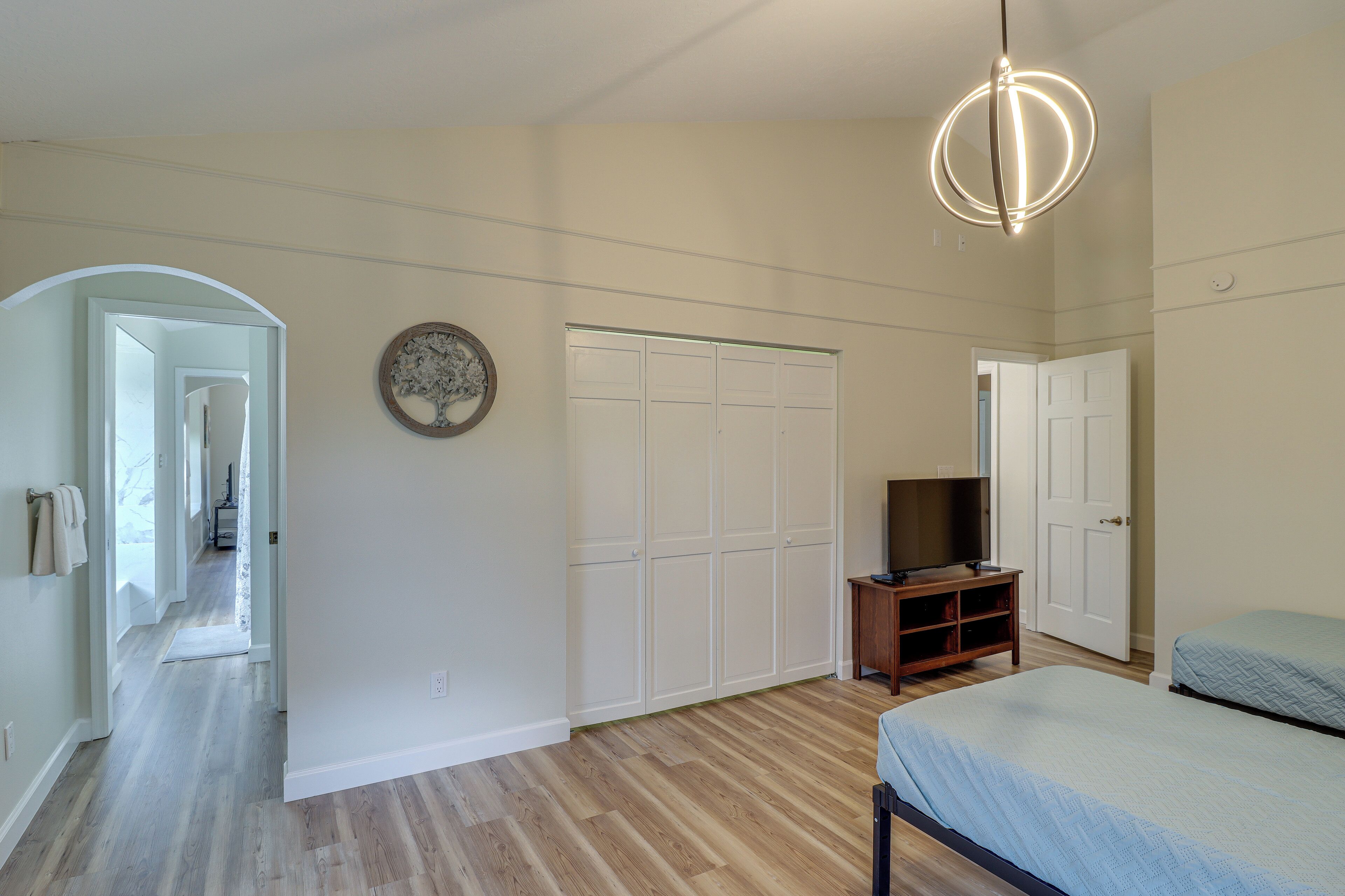 A bedroom with a bed, a TV stand, a wardrobe, and a hallway leading to another room.