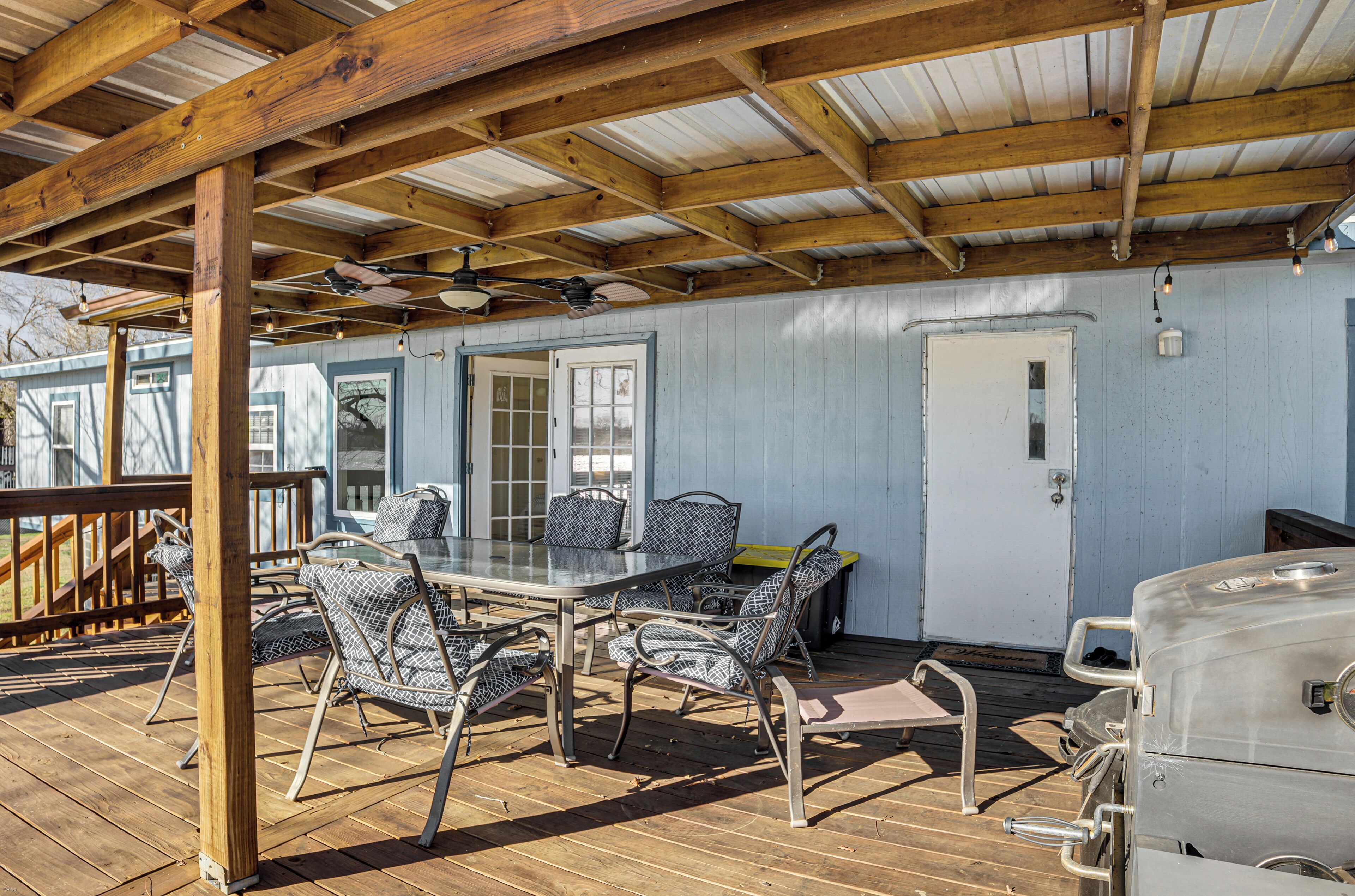 A covered outdoor patio with a table and chairs, a grill, and a door leading to a building.