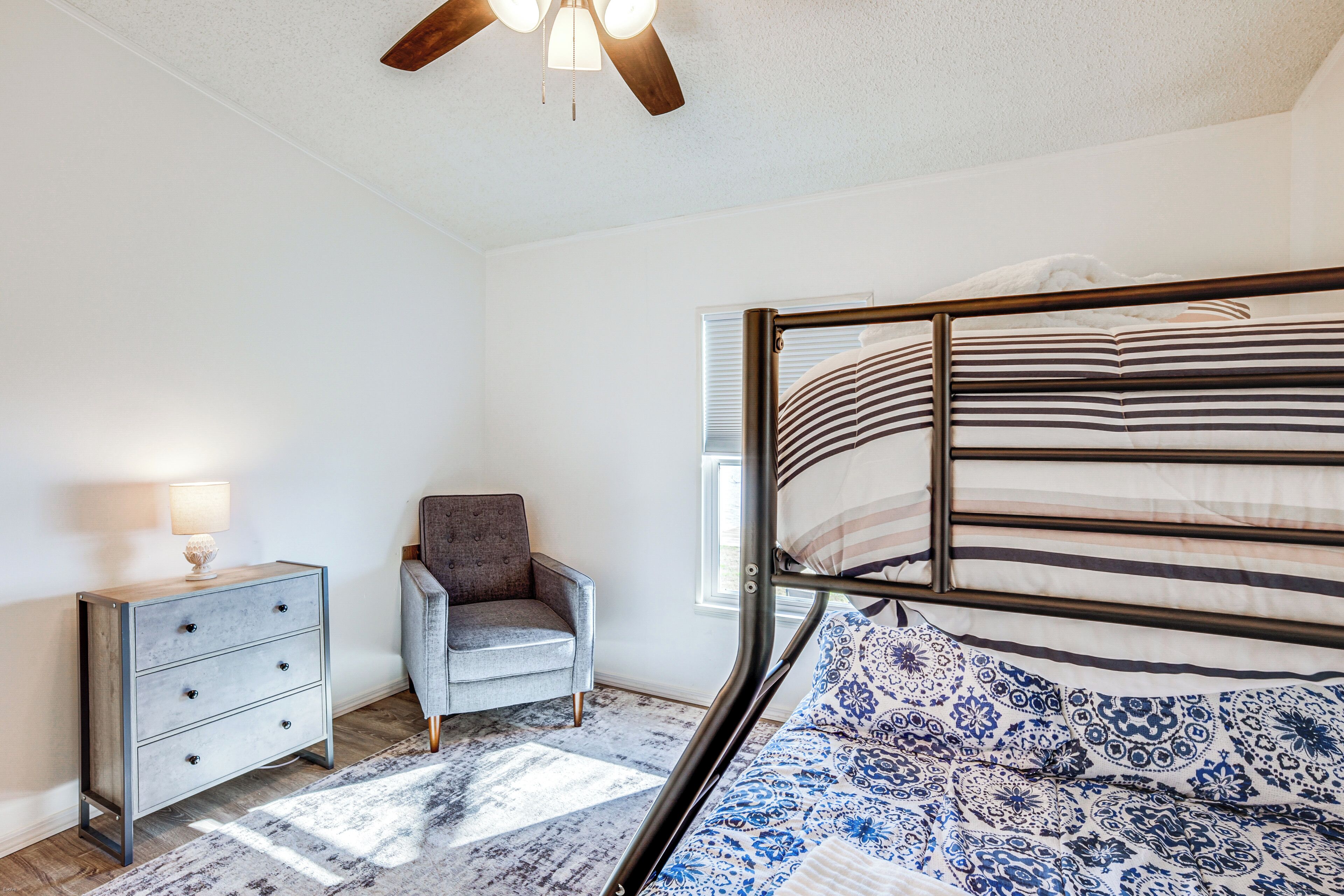 Ein Schlafzimmer mit Etagenbett, Kommode, Stuhl und Deckenventilator.