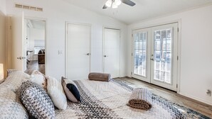 Ein Schlafzimmer mit Bett, Deckenventilator und Blick ins Freie durch eine Glastür.