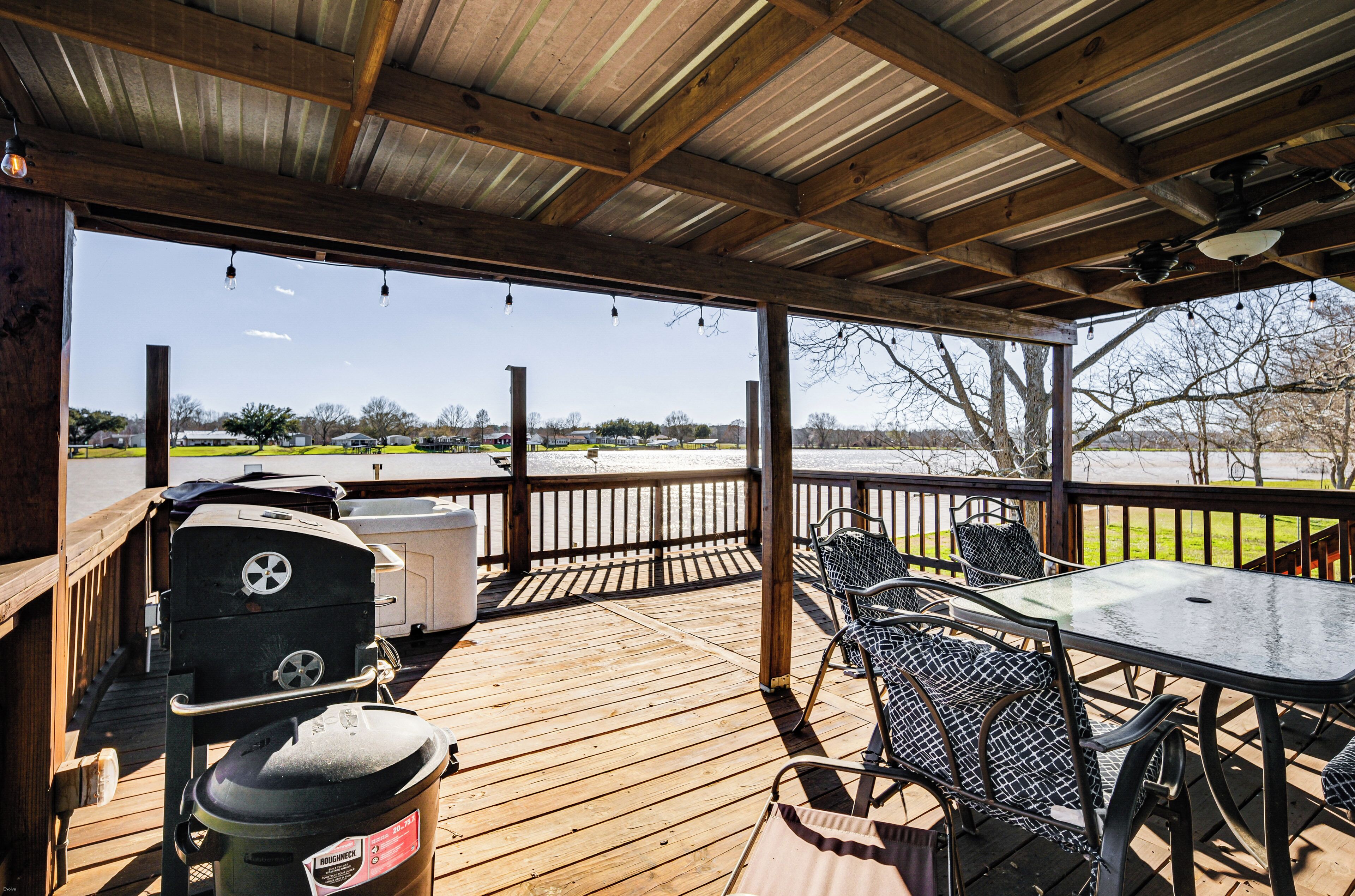 A covered outdoor deck with a grill, chairs, and a table.