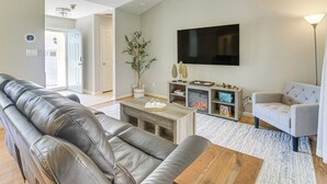 A modern living room with a leather sofa, a wooden coffee table, a grey armchair, and a flat-screen TV mounted on the wall. - Lovely Charlotte Home w/ Yard: 9 Mi to Uptown! (Charlotte)