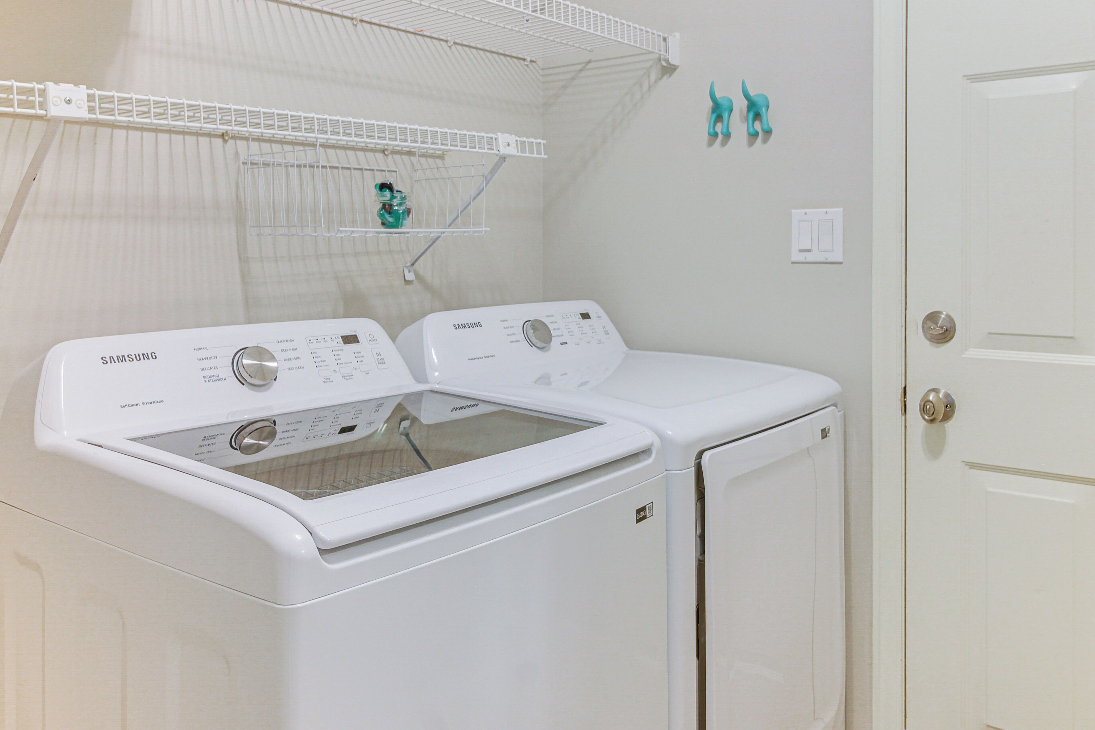 A laundry room with two white Samsung washing machines, a drying rack, and a door with a silver handle.