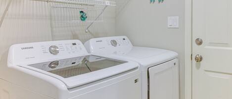 A laundry room with two white Samsung washing machines, a drying rack, and a door with a silver handle.