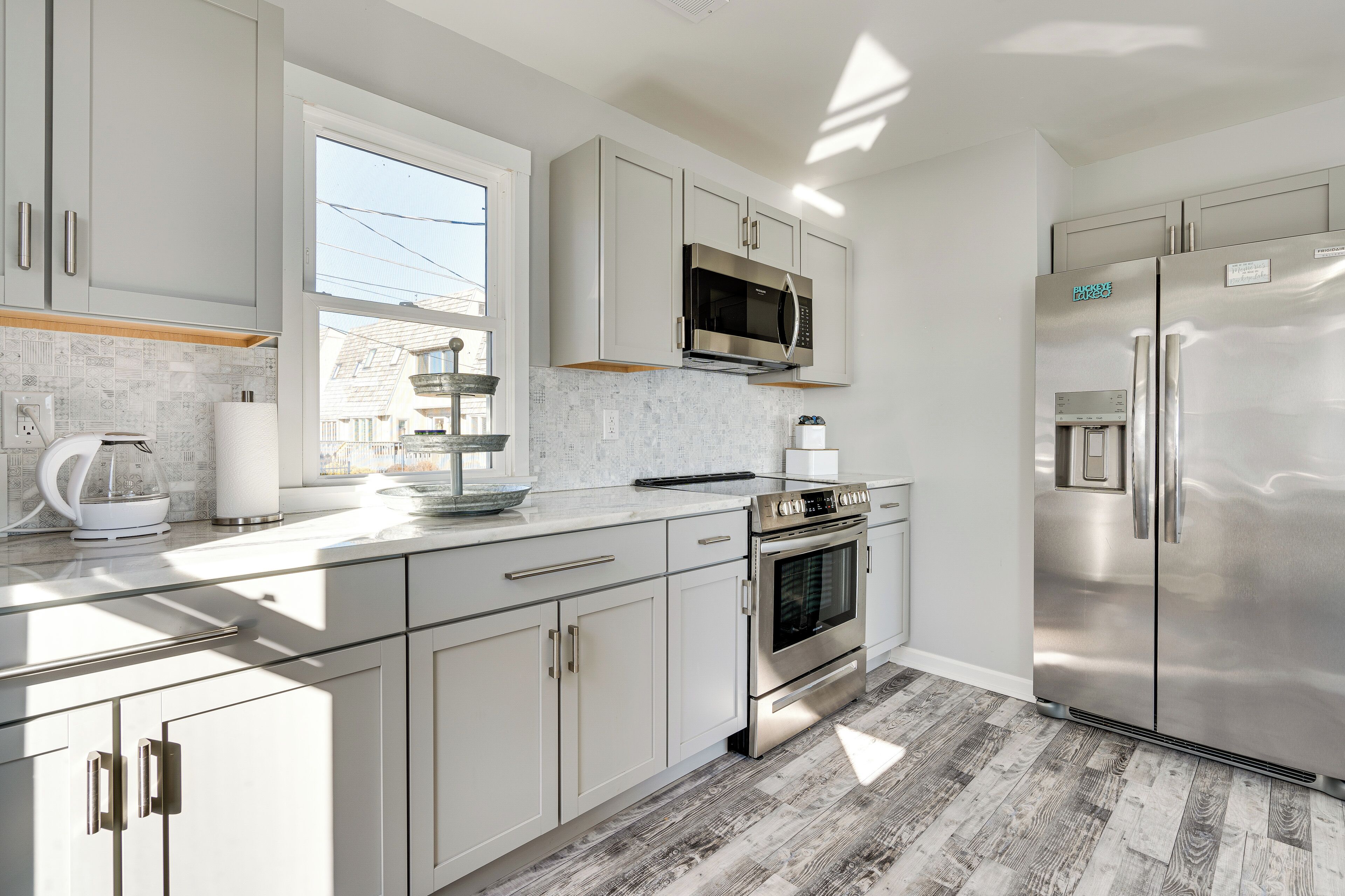 A modern kitchen with stainless steel appliances, white cabinetry, and a window providing natural light.