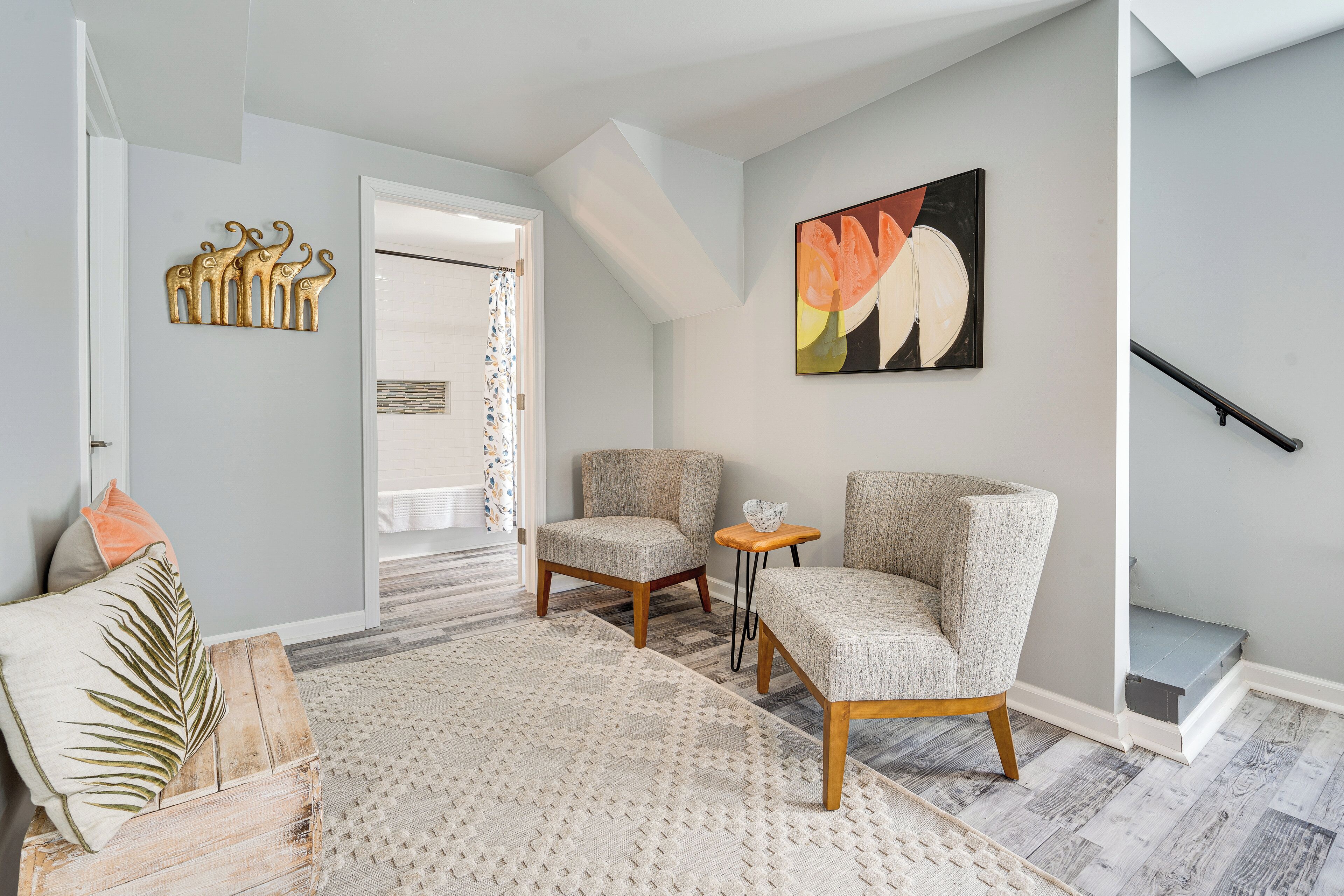A modern living room with a large window, a staircase, and a wall-mounted abstract painting.