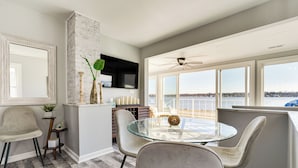 A dining area with a glass table and chairs, a television mounted on the wall, and a view of the water outside. - Waterfront Buckeye Lake Home w/ Deck & Dock! (Buckeye Lake)