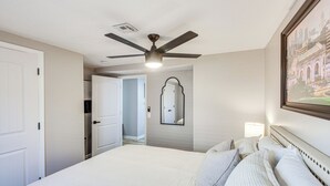 Une chambre d’hôtel avec un lit, un ventilateur de plafond, un miroir et un tableau encadré au mur.