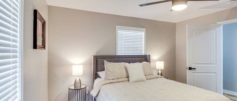 A bedroom with a bed, two bedside lamps, a ceiling fan, and a door.