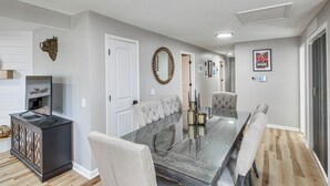 Un coin repas comprenant une table à plateau en verre, des chaises rembourrées, un buffet en bois foncé et un miroir fixé au mur.