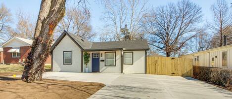 A single-story house with a front yard, a wooden fence, and a tree.