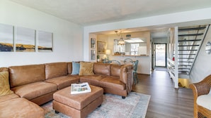 A spacious living room with a brown leather sectional sofa, a coffee table, and a dining area with a chandelier. A staircase leads to an upper level. - Lakefront Moneta Home w/ Community Dock! (Moneta)