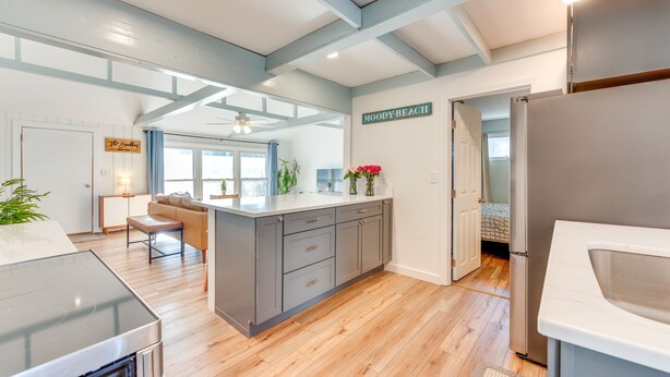 A modern kitchen with a central island, wooden flooring, and a ceiling with exposed beams. - Beautiful Wells Cottage: Steps to Moody Beach! (Wells)