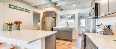 A modern kitchen with a central island, grey cabinets, and a sign reading "MOODY BEACH".
