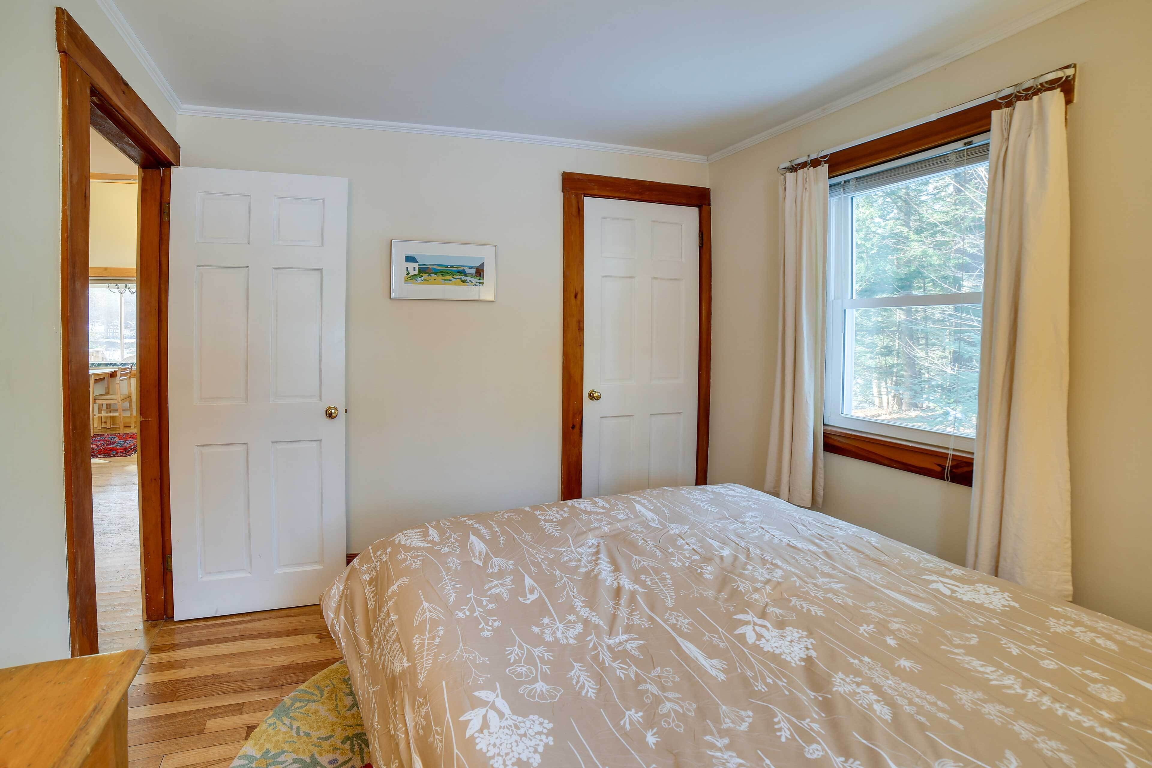 A bedroom with a bed, two doors, a window, and a small picture on the wall.
