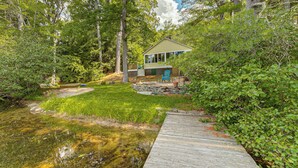 A house with a deck, surrounded by dense greenery and a small pond. - Lakefront Bradford Cottage w/ Dock, Near Skiing! (Bradford)
