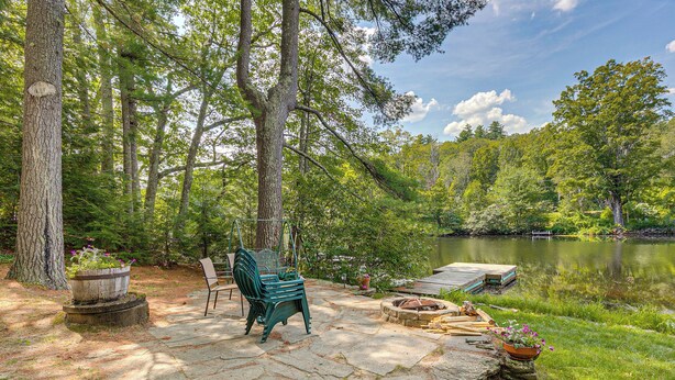 A stone patio with a green chair and a wooden bench, surrounded by trees and a lake. - Lakefront Bradford Cottage w/ Dock, Near Skiing! (Bradford)