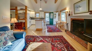 A spacious living room with a fireplace, a blue sofa, and a kitchen in the background. - Lakefront Bradford Cottage w/ Dock, Near Skiing! (Bradford)