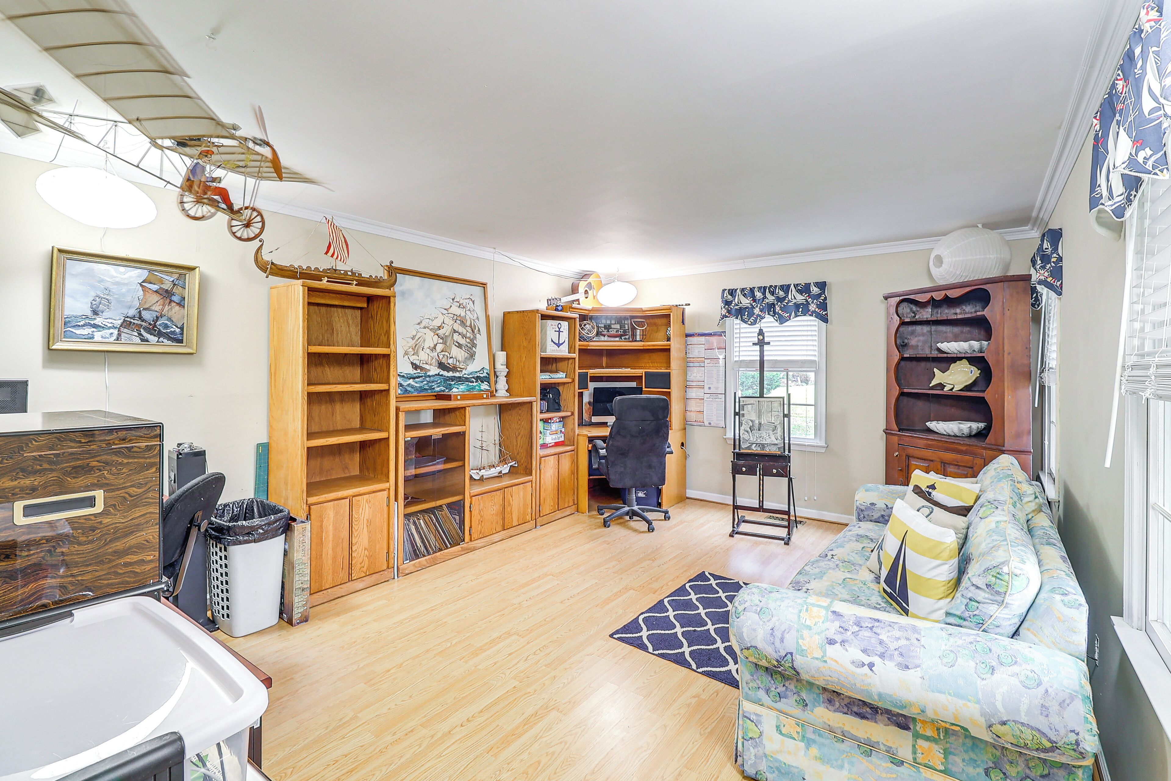 A room with a wooden desk, a computer, a bookshelf, a couch, and a sailboat model.