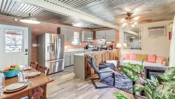 Een moderne keuken met roestvrijstalen apparatuur, een eethoek met een houten tafel en een woonkamer met een bank en planten.