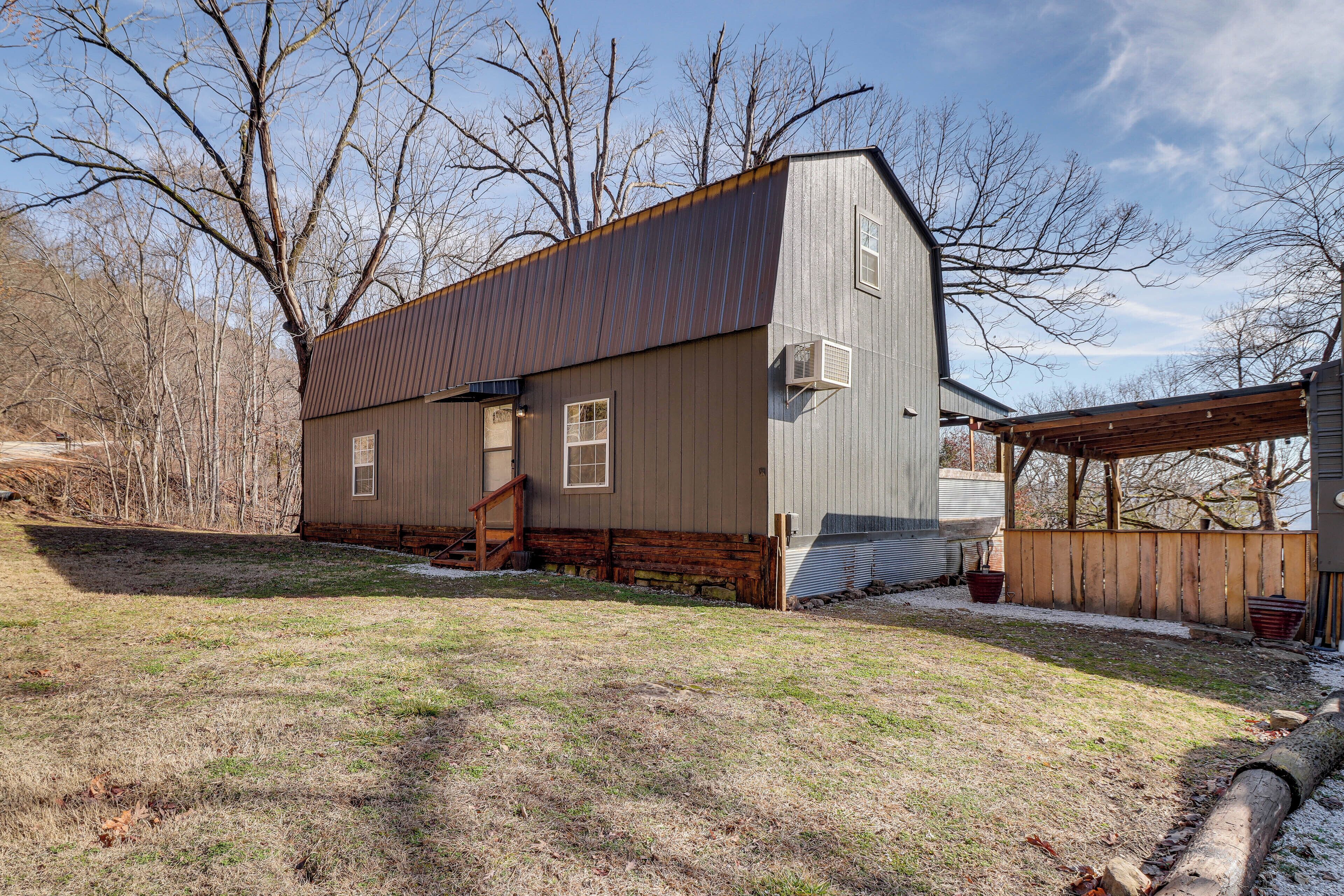 A two-story building with a metal roof and wooden siding, a wooden deck, and a stone foundation.