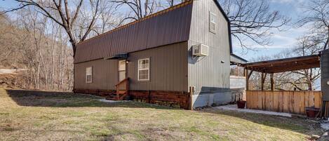 A two-story building with a metal roof and wooden siding, a wooden deck, and a stone foundation.