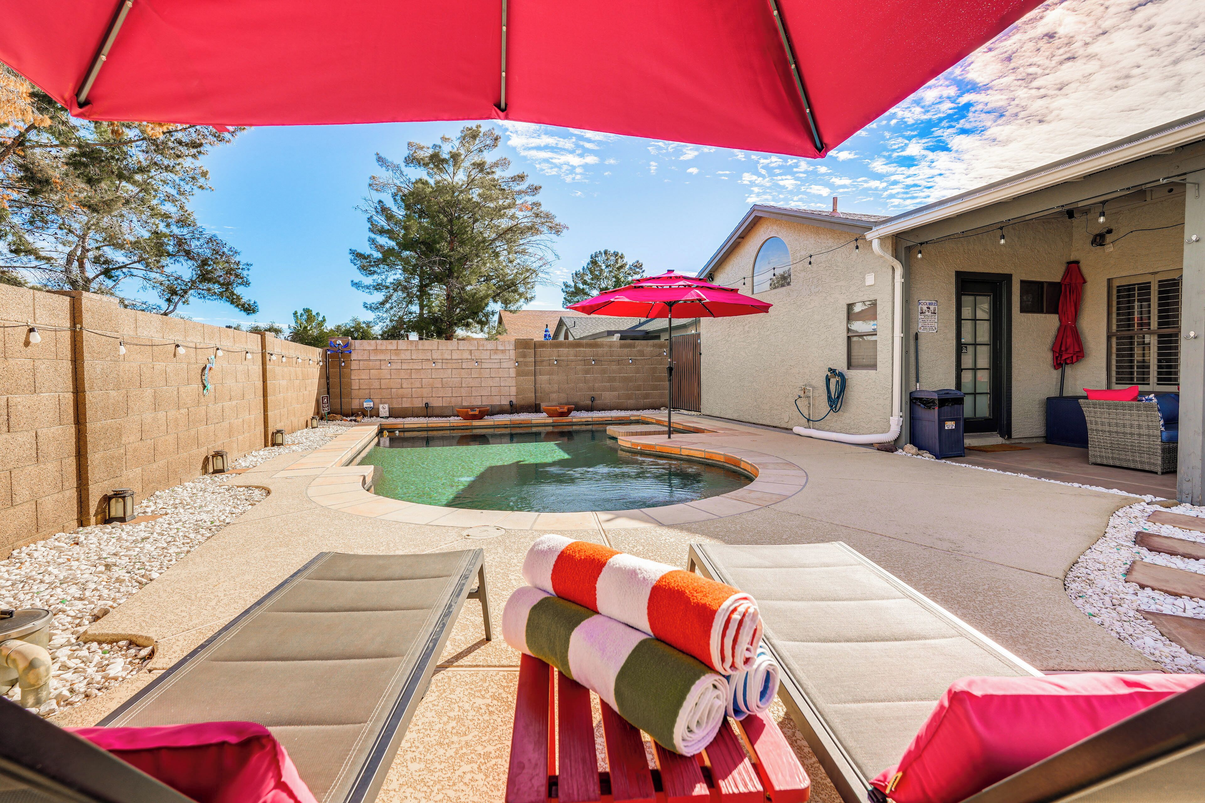A backyard with a swimming pool, lounge chairs, and a red umbrella.