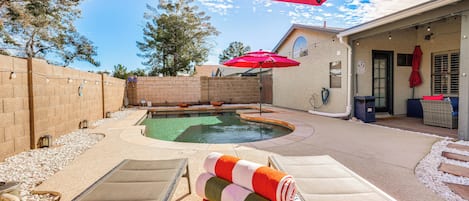 A backyard with a swimming pool, lounge chairs, and a red umbrella.