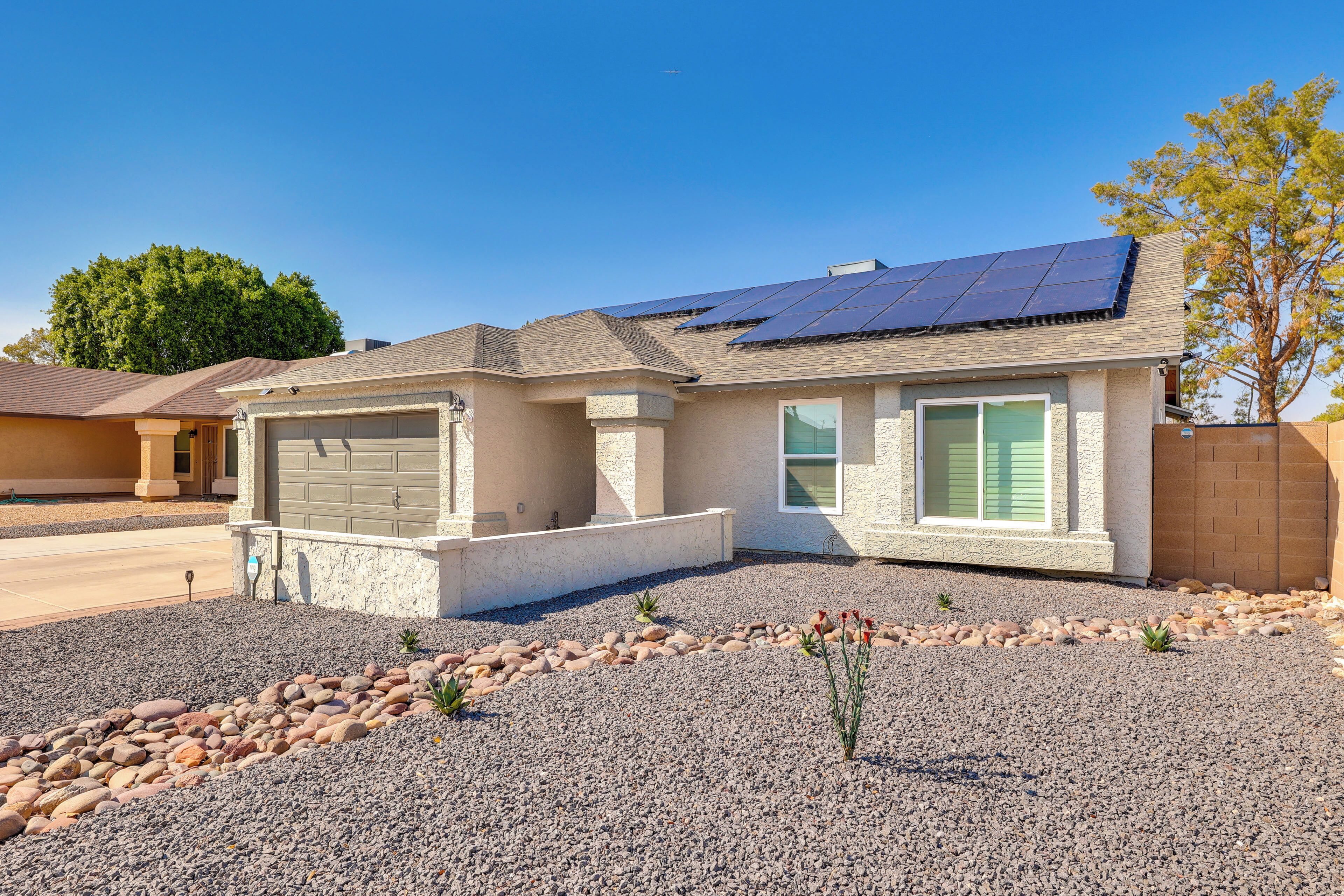 A single-story house with a garage, a solar panel roof, and a gravel driveway.