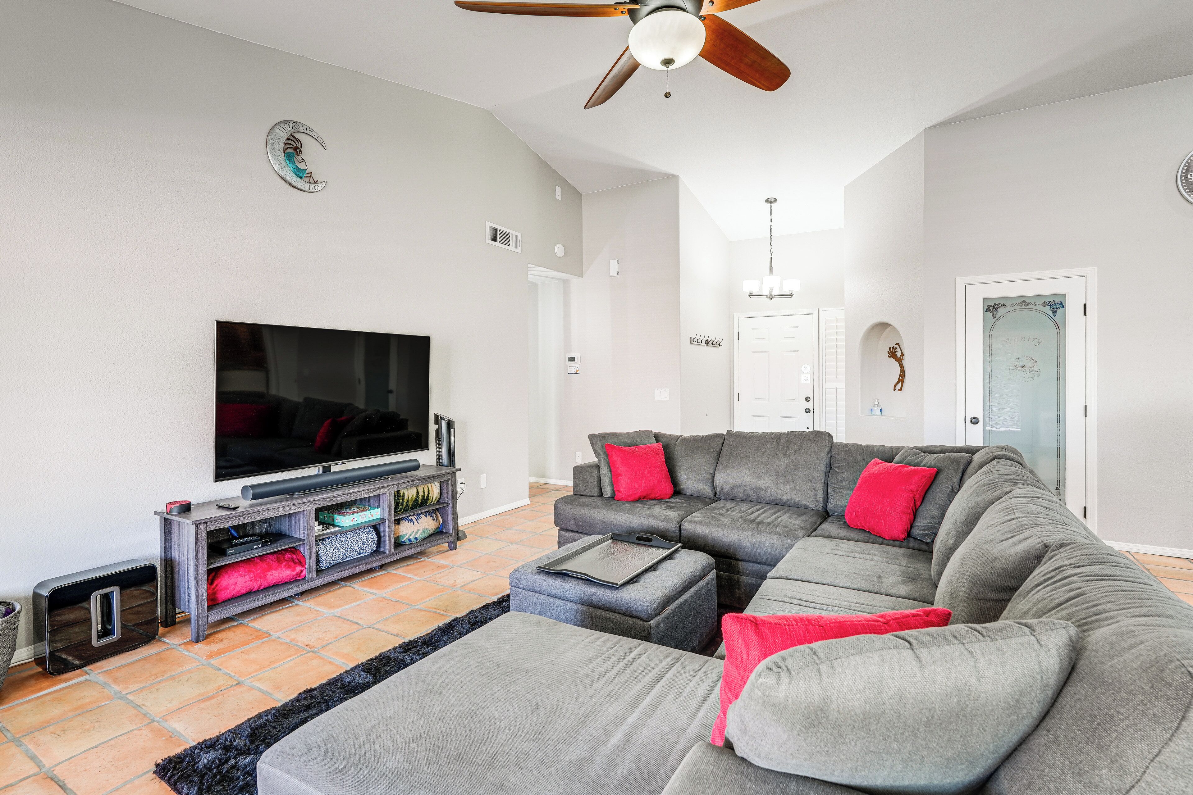 A modern living room with a sectional sofa, a flat-screen TV, and a ceiling fan.
