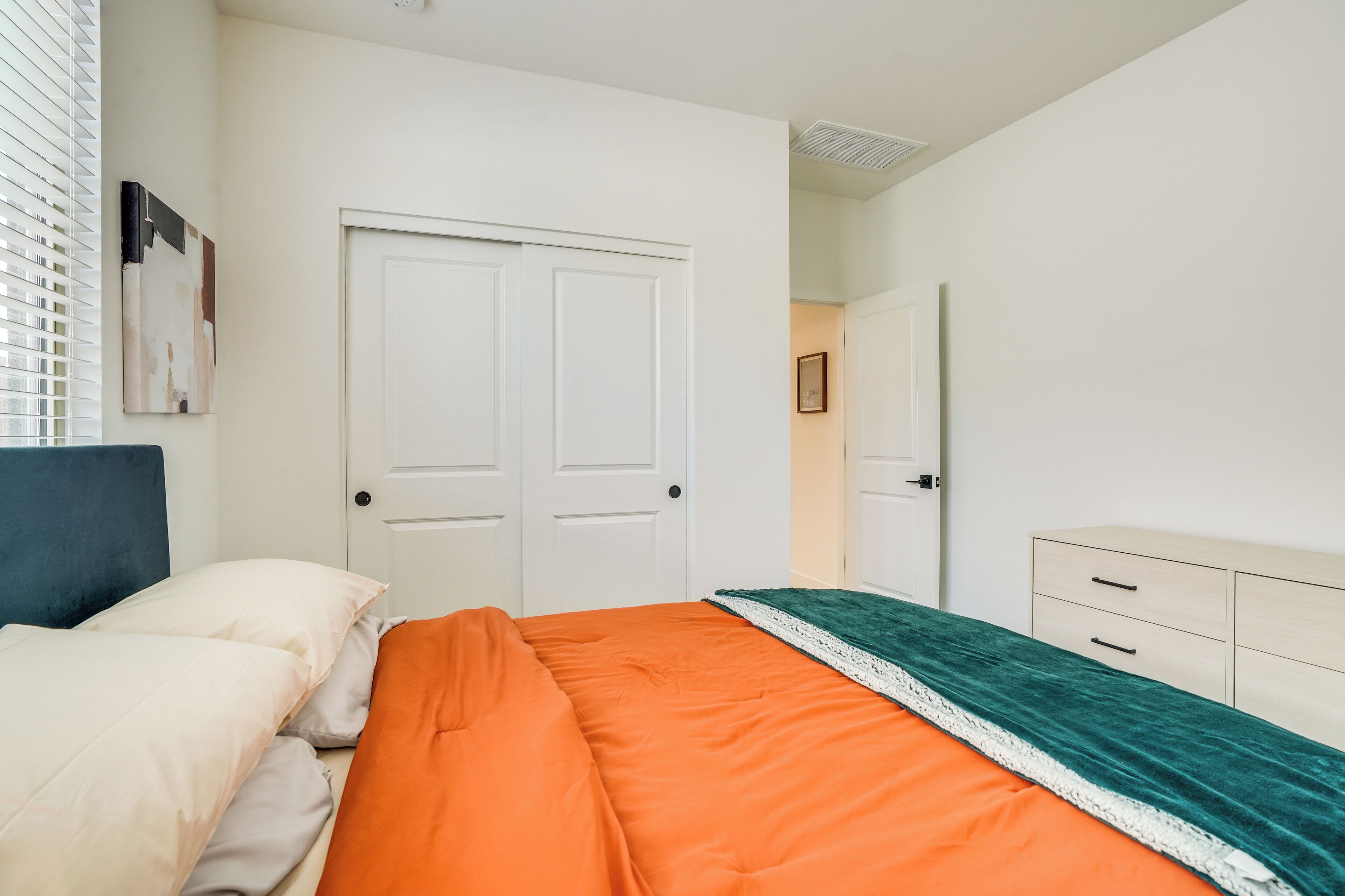 Un dormitorio con cama, dos puertas blancas, cómoda y ventana con persianas.