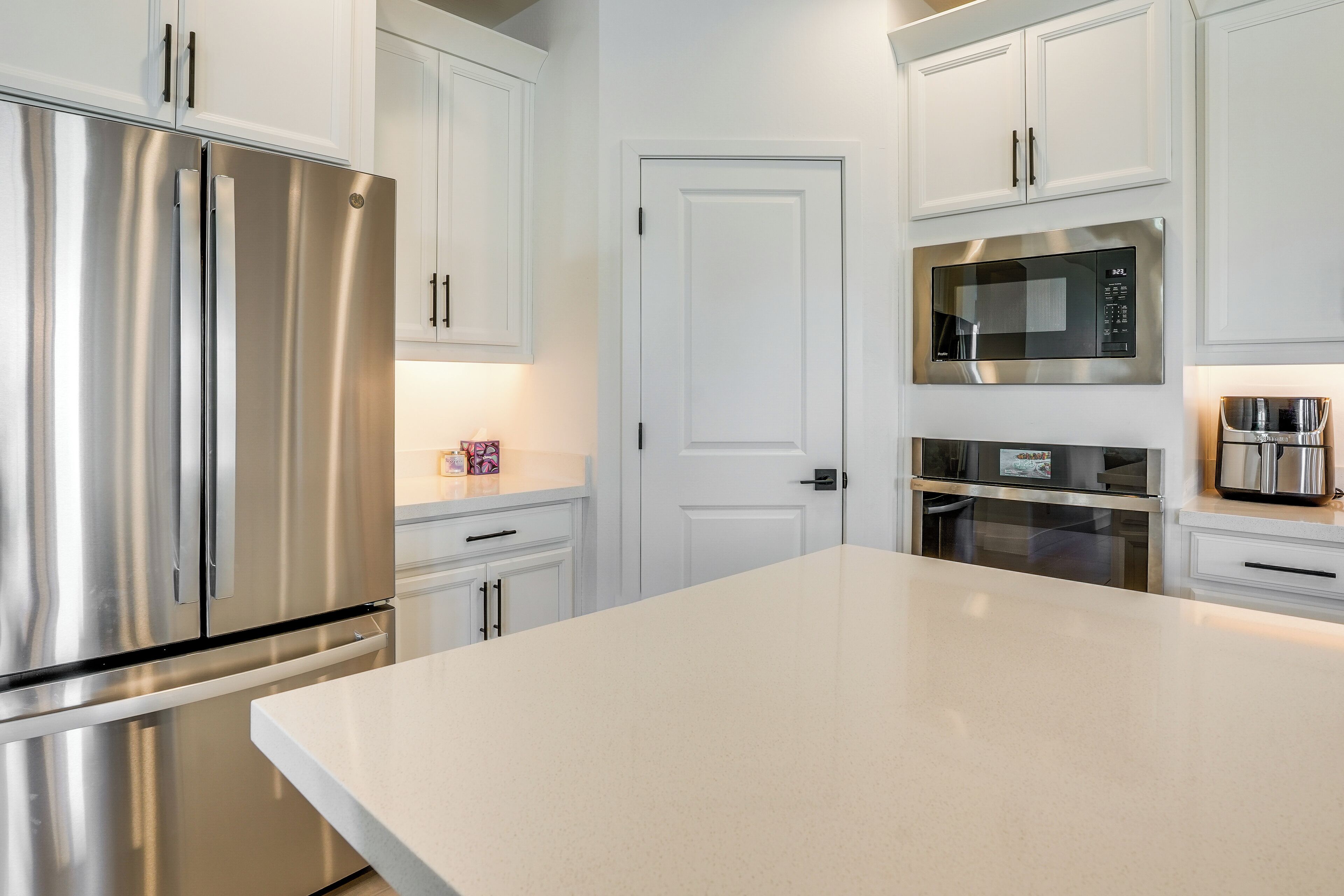 A modern kitchen with stainless steel appliances, white cabinetry, and a large countertop.