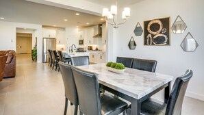 A modern kitchen with white cabinets, a stainless steel refrigerator, and a dining area with a marble table and leather chairs. - 5 Mi to Westgate! Newly Built Family Retreat (Glendale)