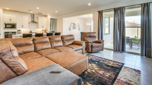A modern living room with a leather sectional sofa, a dining area with a table and chairs, and a kitchen with white cabinets and stainless steel appliances. - 5 Mi to Westgate! Newly Built Family Retreat (Glendale)