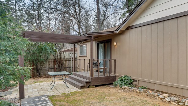A covered patio with a table and chairs, a wooden deck, and a stone border. - Charming Lakehead Cabin: Walk to Shasta Lake! (Lakehead)
