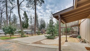 A covered patio area with a concrete floor, surrounded by trees and a wooden fence. - Charming Lakehead Cabin: Walk to Shasta Lake! (Lakehead)