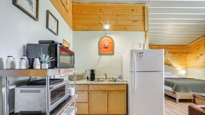 A compact kitchen with a refrigerator, microwave, and toaster oven. There is a sink with a faucet and a wooden countertop. A bed is visible in the background with a green blanket. - Waynesville Studio w/ Fire Pit & Mountain Views! (Waynesville)