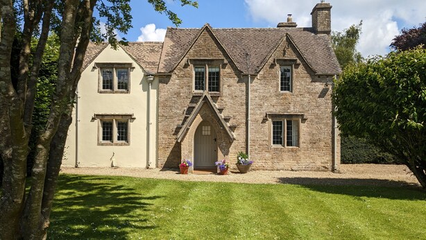 A stone house with a gabled roof, a central entrance, and a small porch with potted plants. - Charlton Down Cottage - Westonbirt - Pet Friendly (Westonbirt)