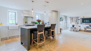 Et moderne køkken med en central ø, barstole og et spiseområde med et fjernsyn og siddepladser.