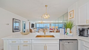 Una cocina moderna con una isla grande, armarios blancos, tiradores dorados y lavavajillas integrado.